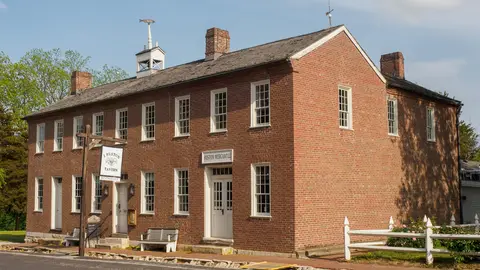 The two-story red brick J. Huston Tavern on Main Street in Arrow Rock, Missouri, with a small white cupola on the roof and a wooden sign by the door