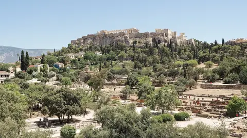 The Acropolis on its rock above the green, tree-filled Ancient Agora of Athens on a clear day, with the small Byzantine Church of the Holy Apostles among the ruins