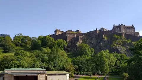 Edinburgh Castle on its volcanic rock above the trees and lawns of West Princes Street Gardens on a sunny evening