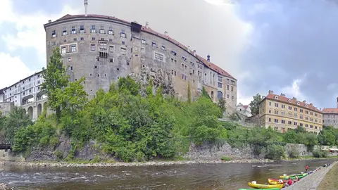Český Krumlov Castle rising from a wooded rock above the Vltava, the painted Castle Tower on the right and canoes pulled up on the riverbank