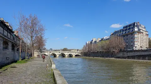 People walking along the cobbled Seine quay toward the Pont Neuf in Paris on a clear spring day
