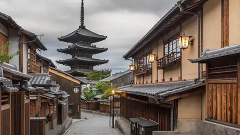 Yasaka-dori in Kyoto's Higashiyama district early in the morning, with lit lanterns on wooden townhouses and the five-storey Yasaka Pagoda at the top of the lane
