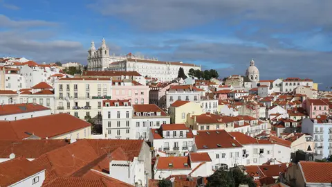 Red-tiled roofs of Alfama in Lisbon seen from the Miradouro de Santa Luzia, with the white towers of São Vicente de Fora and the dome of Santa Engrácia on the skyline