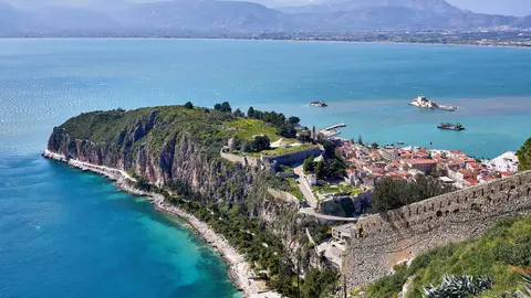 The green Akronafplia headland and the red roofs of Nafplio's old town seen from the walls of Palamidi, with the Bourtzi islet fortress in the bay and mountains across the Argolic Gulf