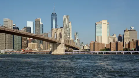 The Brooklyn Bridge crossing the East River toward the Lower Manhattan skyline and One World Trade Center on a clear morning