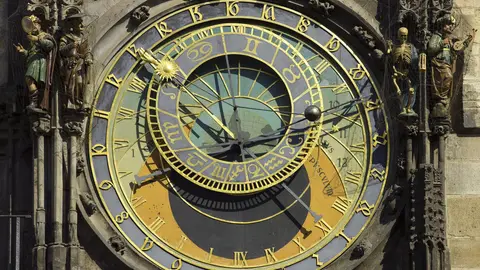 The gold and blue astronomical dial of the Prague Astronomical Clock on the Old Town Hall, with carved figures, including a skeleton, on either side