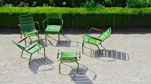 Green metal chairs in a loose circle on the gravel of the Jardin des Tuileries in Paris, with a trimmed hedge behind