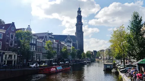 The Prinsengracht canal in Amsterdam on a sunny day, with moored boats, gabled canal houses and the tall Westerkerk tower at the end