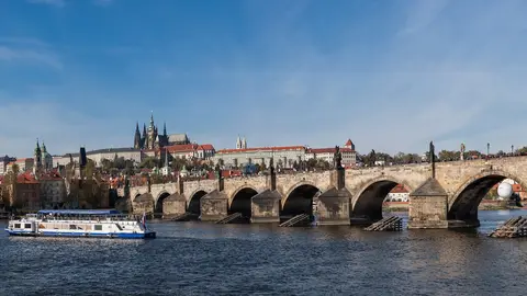 Charles Bridge crossing the Vltava with Prague Castle and St. Vitus Cathedral on the hill behind, a river boat in front