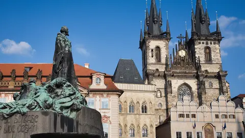 The Jan Hus Memorial in front of the twin Gothic spires of Týn Church on Prague's Old Town Square under a blue sky