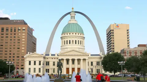 The green-domed Old Courthouse in St. Louis with the Gateway Arch rising behind it, seen across the fountain and runner statue in Kiener Plaza