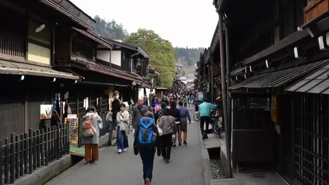 Visitors walking down Kamisannomachi in Takayama's old town, between dark wooden merchant houses with a stone water channel running along the street