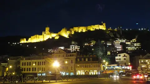 Narikala Fortress lit up gold on the hill above the old town houses of Tbilisi at night