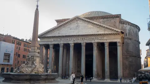 The Pantheon's columned portico and dome in early morning light, with the obelisk fountain of Piazza della Rotonda in front and a few people crossing the square